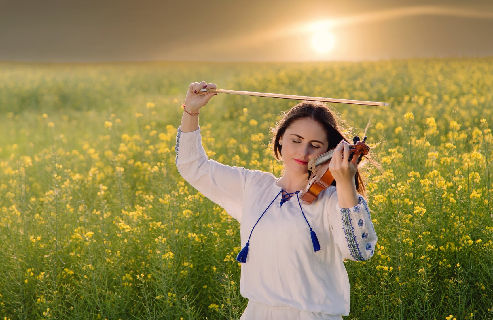 Young woman playing violin in a field at sunset