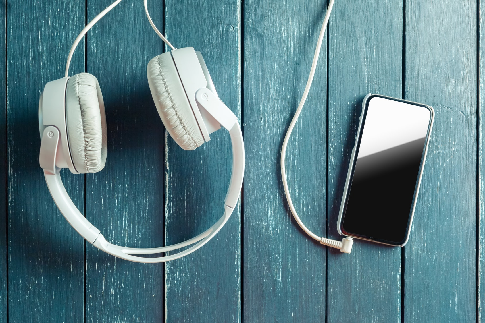 white earphones attached to smartphone on wooden background